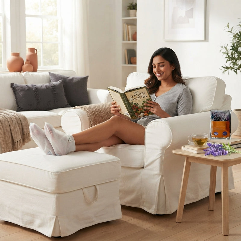 South Asian woman wearing hydrating exfoliating foot mask socks while relaxing in a sunlit room.